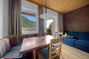 A room with a wooden table, a bench, a sofa, and a view of a mountain.