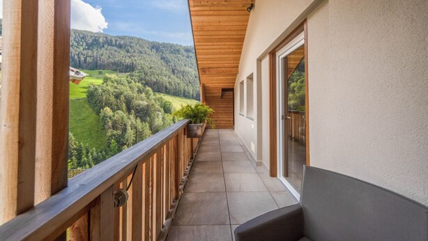 Un balcone affaccia su un paesaggio verde e presenta un soffitto in legno.