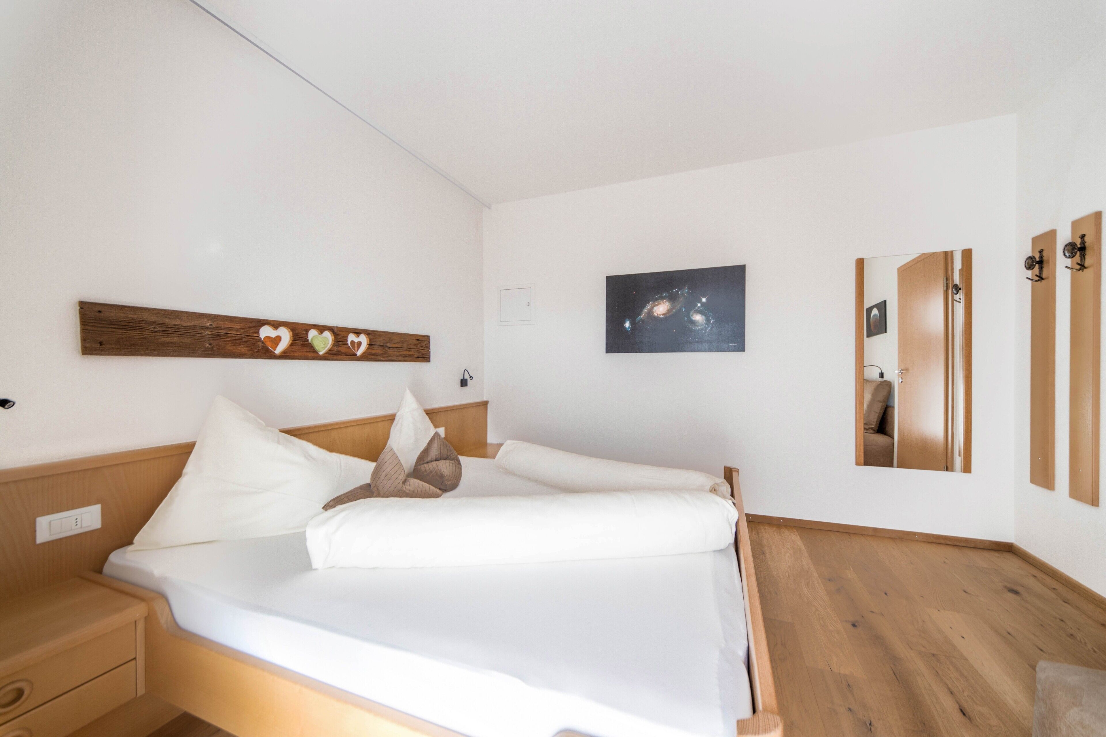 Een slaapkamer met een bed, een houten hoofdbord, wit beddengoed, een aan de muur hangend schilderij en een houten vloer.