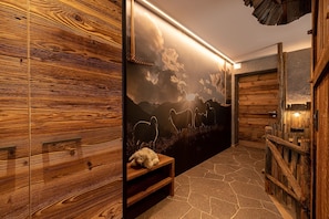 Un intérieur en bois avec un sol en pierre, un banc et une fresque murale représentant un paysage de montagne.