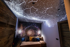 A room with a starry ceiling projection, a galaxy-themed wall mural, and a brown sofa with cushions.