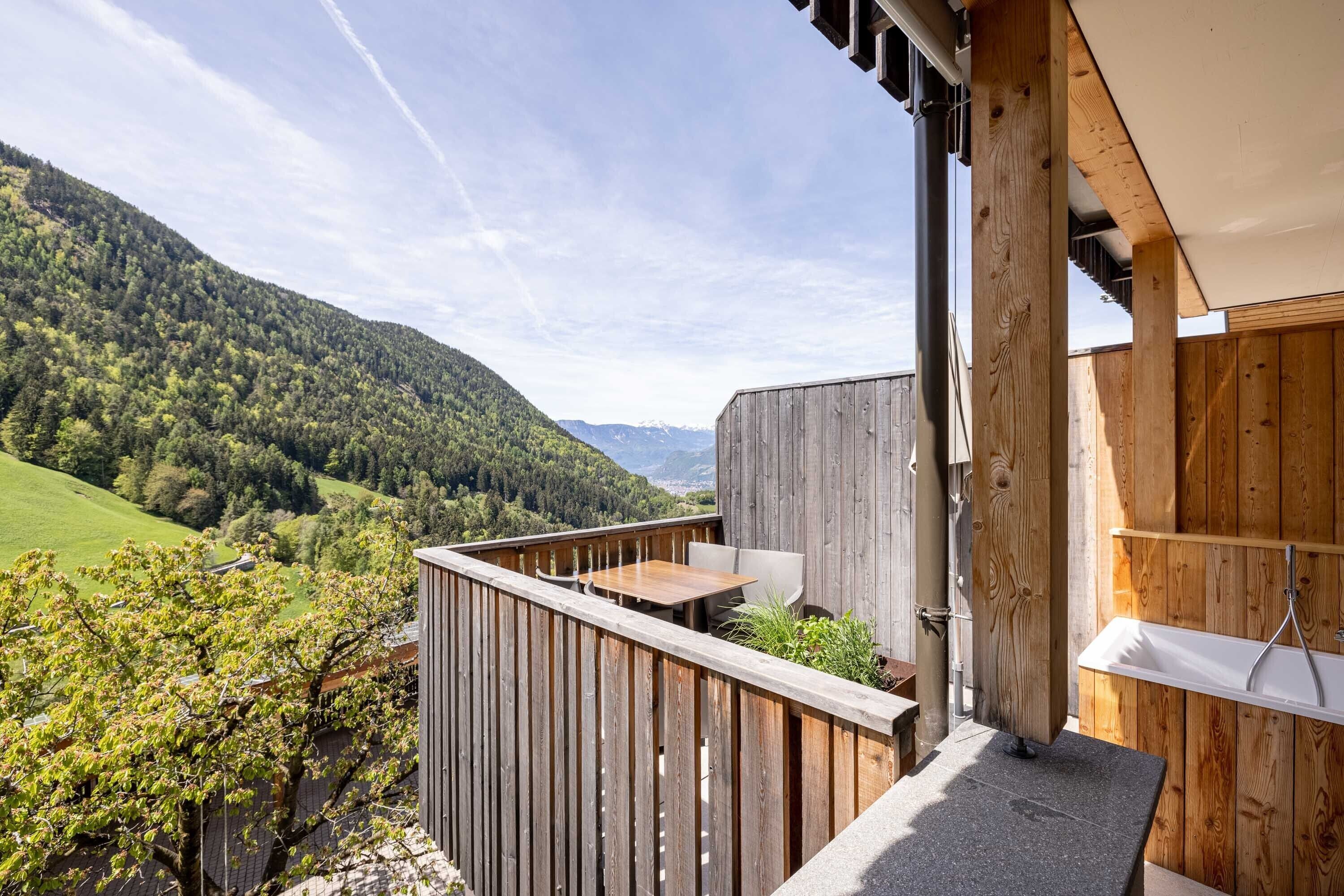 Un balcon en bois, agrémenté d’une table et de chaises, qui offre une vue sur un paysage montagneux.