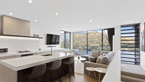 Eine moderne Küche mit einer zentralen Kochinsel, Barhocker, einem Flachbildfernseher und großen Fenstern mit schöner Aussicht.