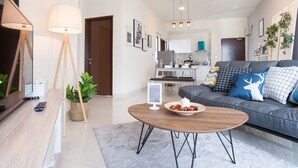 A modern living room with a sofa, coffee table, and floor lamp. A kitchen is visible in the background.