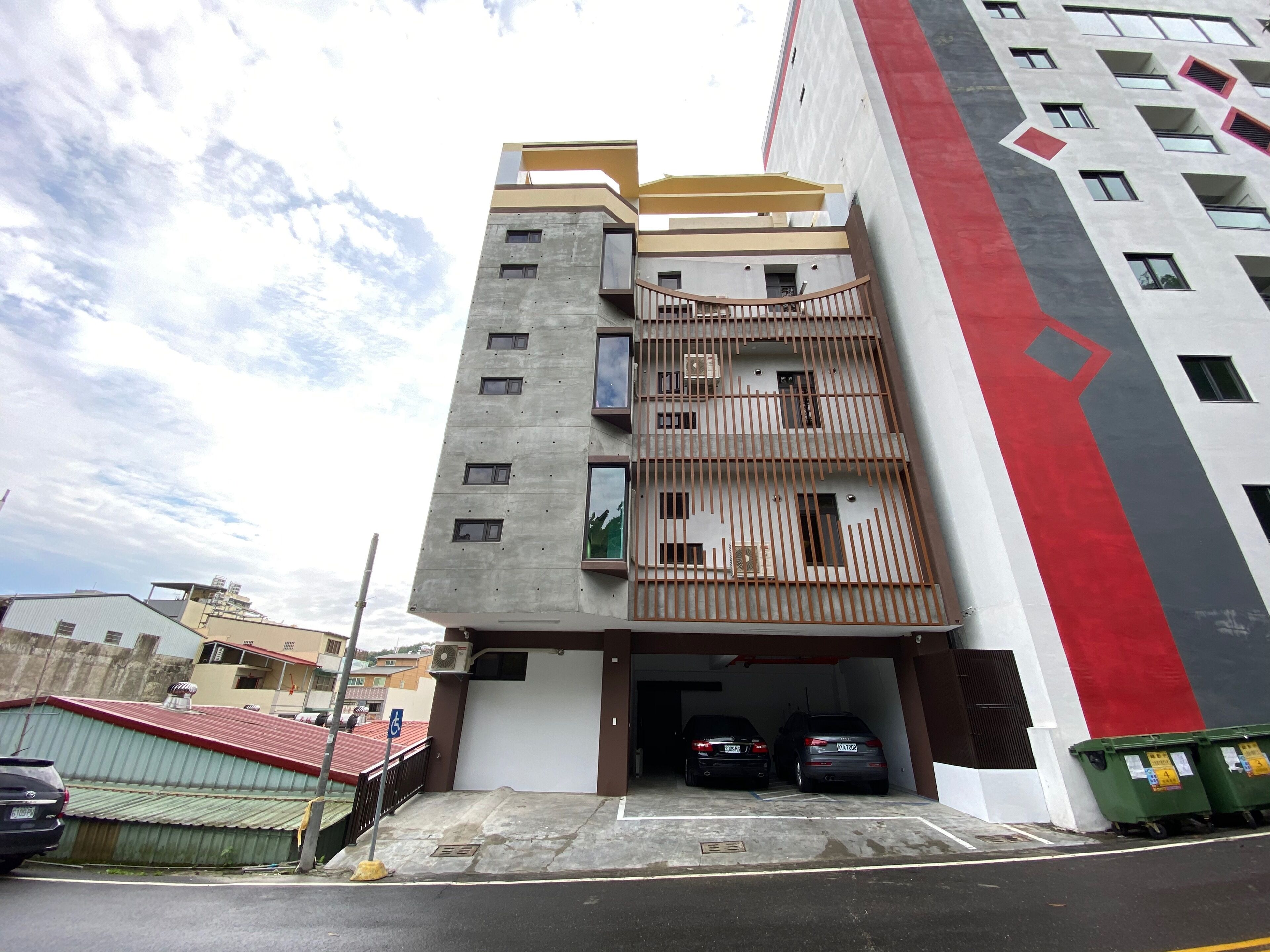 A multi-story building with a parking garage entrance, two cars parked inside, and a red and grey facade.
