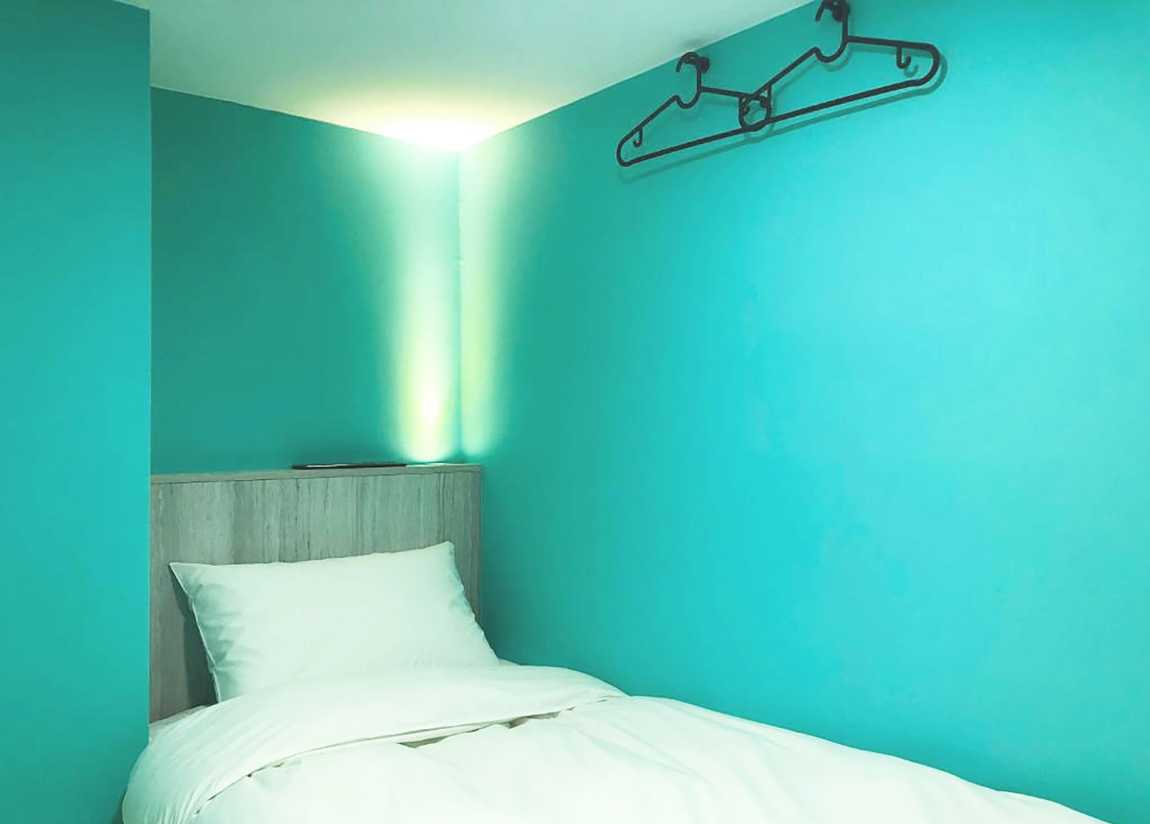 Un lit simple avec une tête de lit en bois, dans une pièce aux murs de couleur turquoise et dotée d’un porte-manteau suspendu.