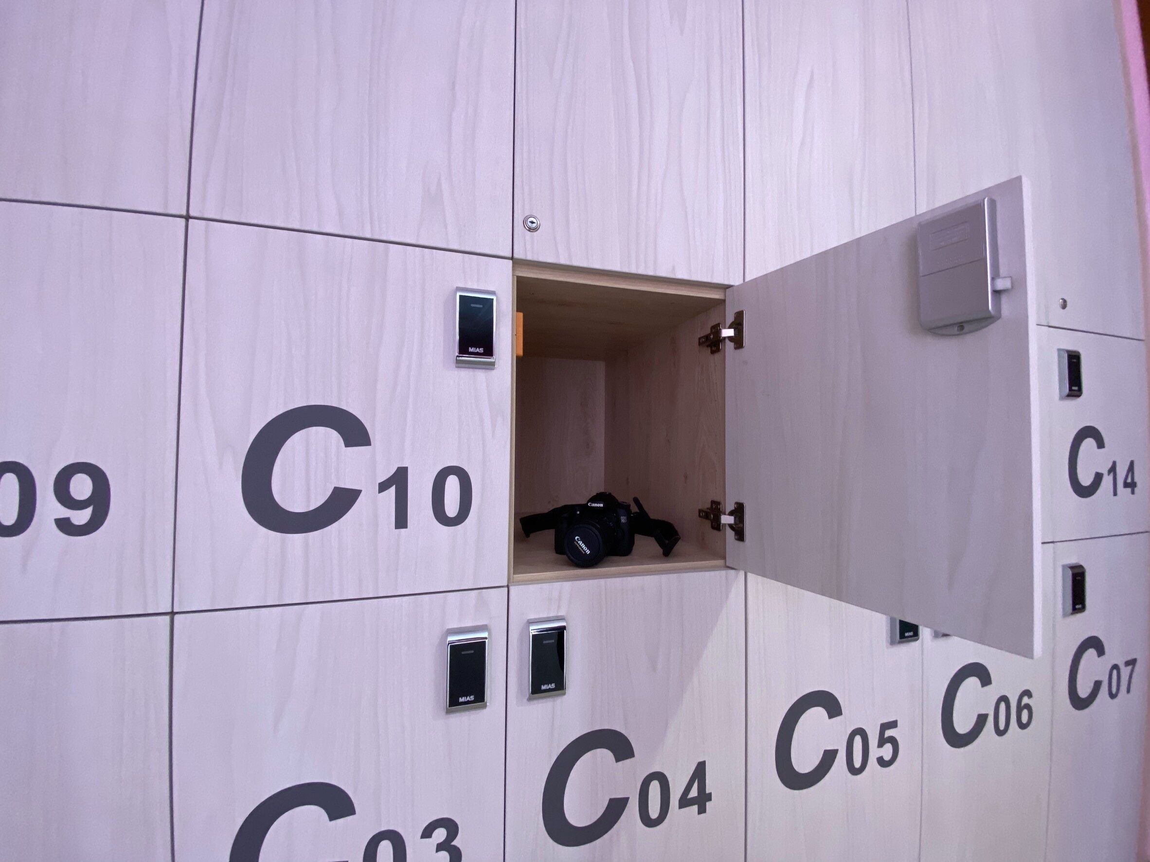 Een rij lockers met nummers C03 tot C14, waarvan enkele met MIAS-sloten, en een camera in één locker.