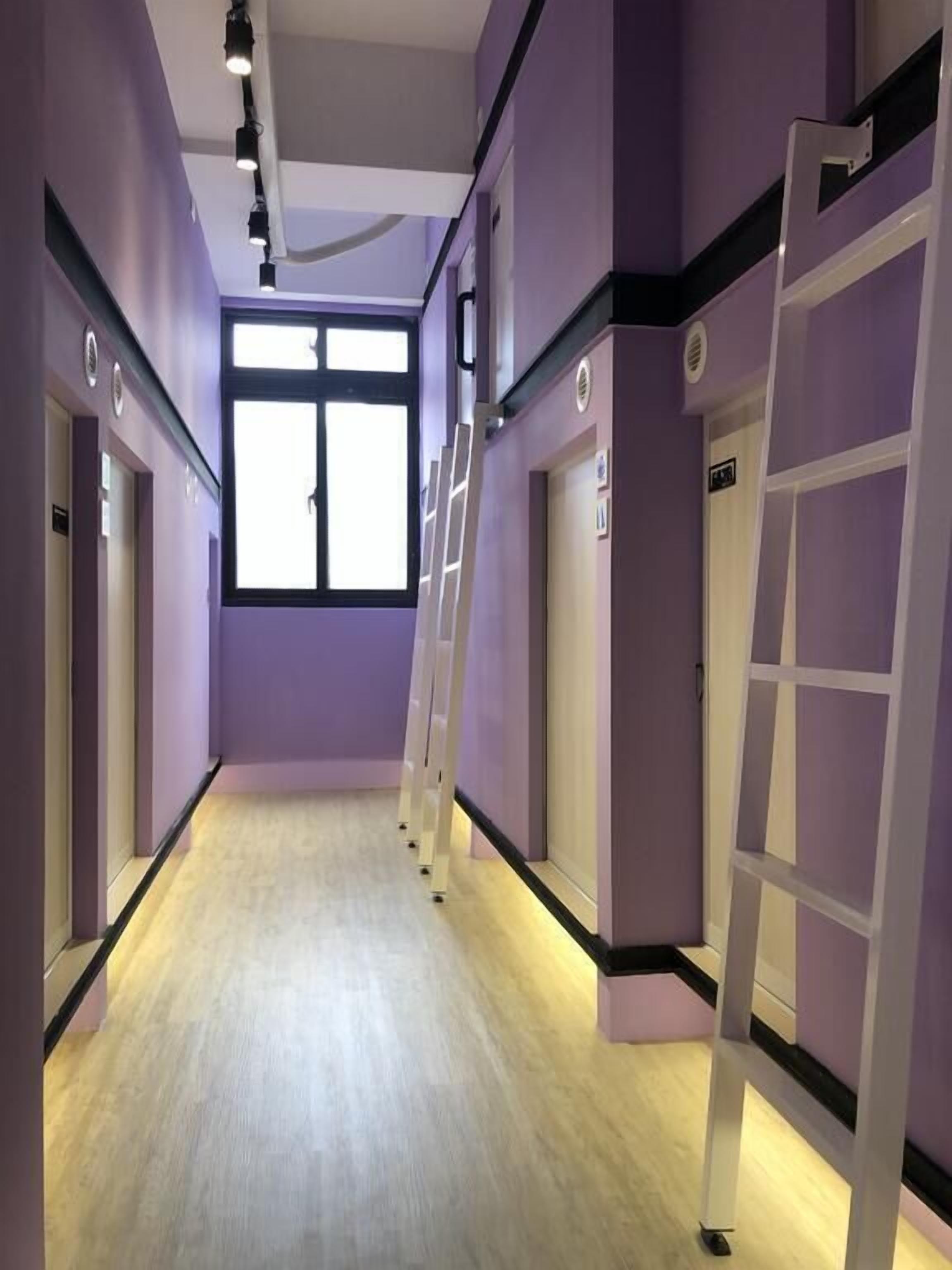 A hallway with purple walls, a wooden floor, and a window at the end.