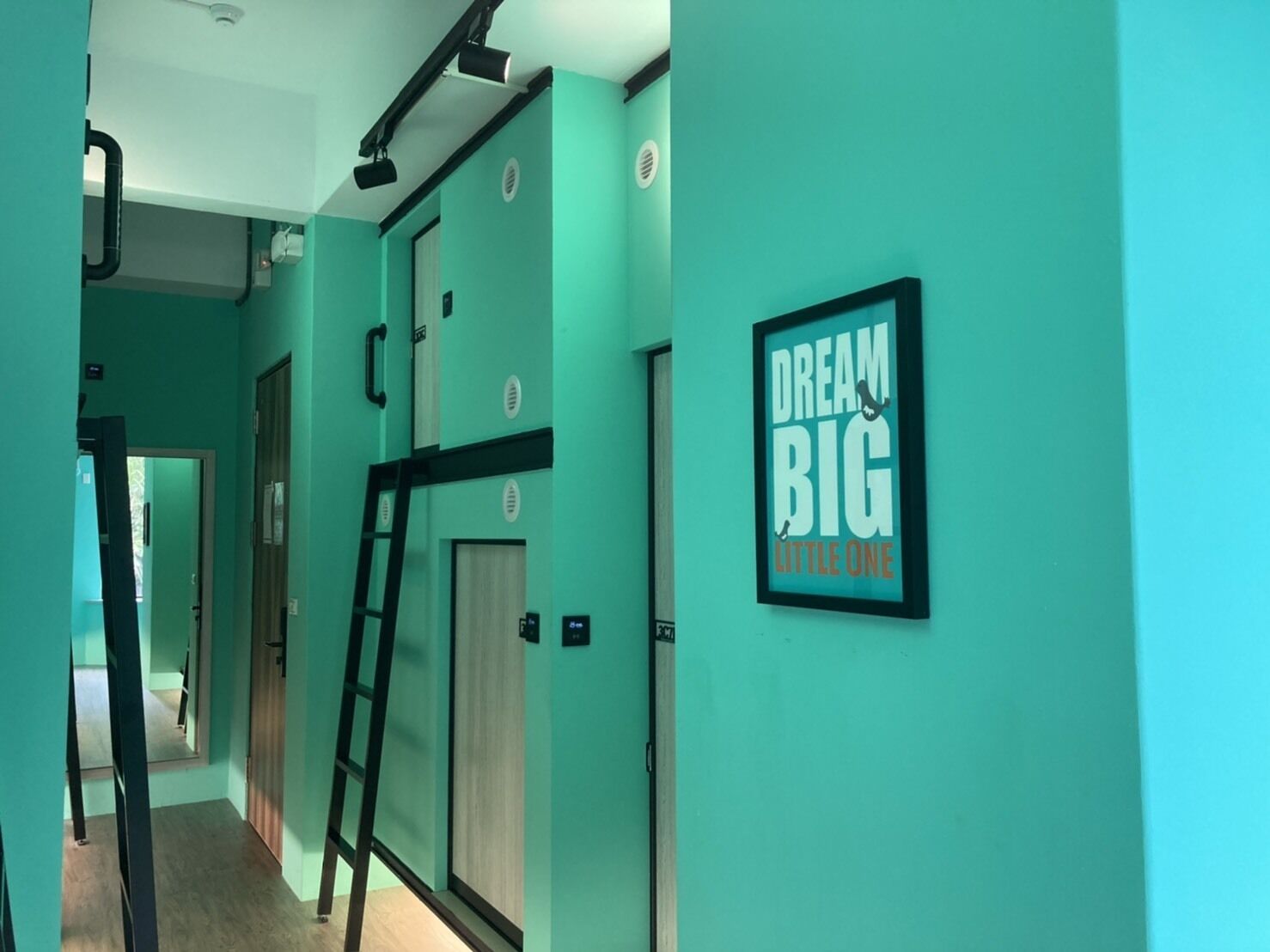 Een gang met turquoise muren, een ingelijst motiverend citaat en een ladder tegen de muur.