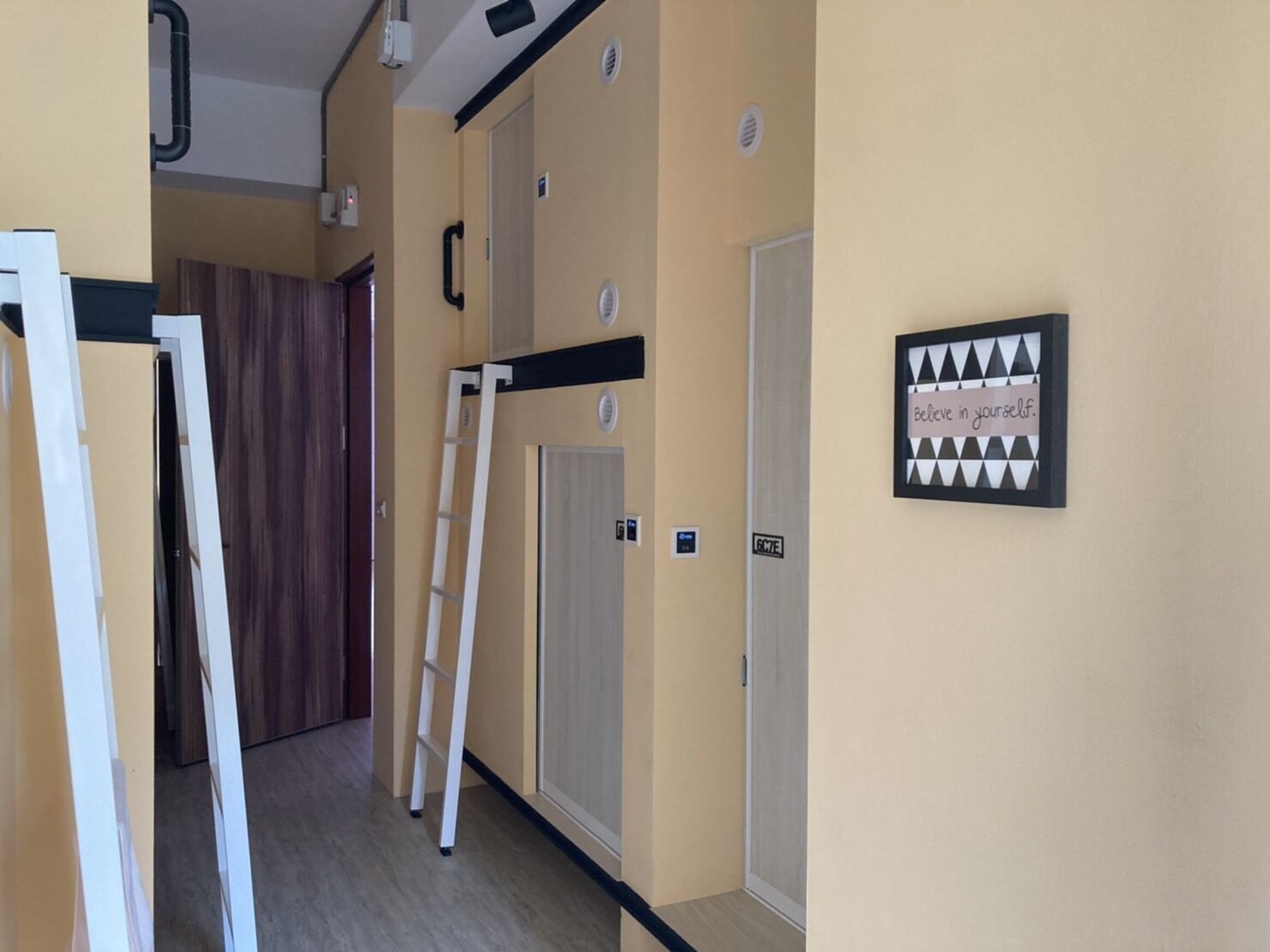 A hallway with a wooden door, a white ladder, and a motivational sign on the wall.