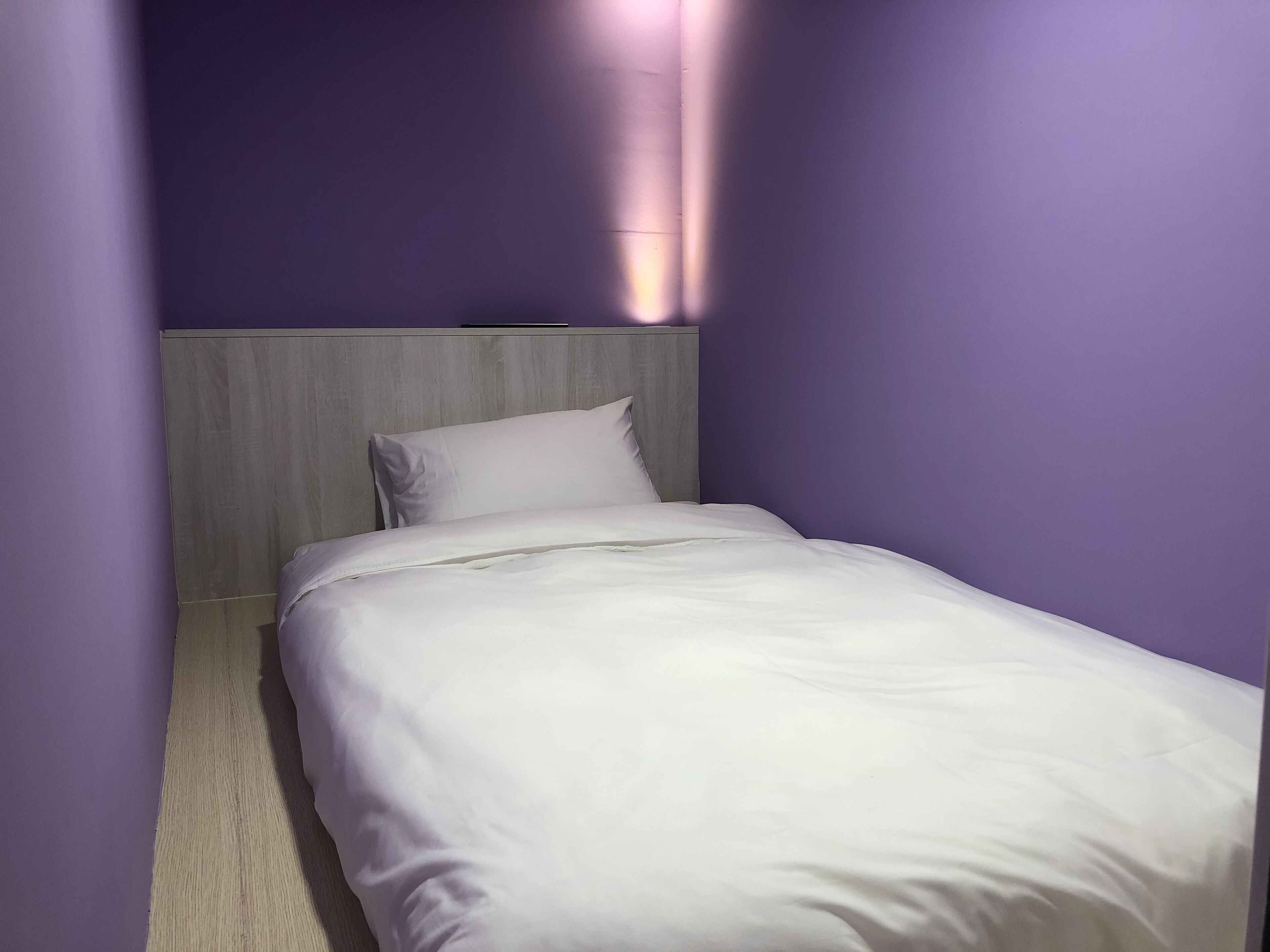 A small, neatly made bed in a room with purple walls and a wooden headboard.