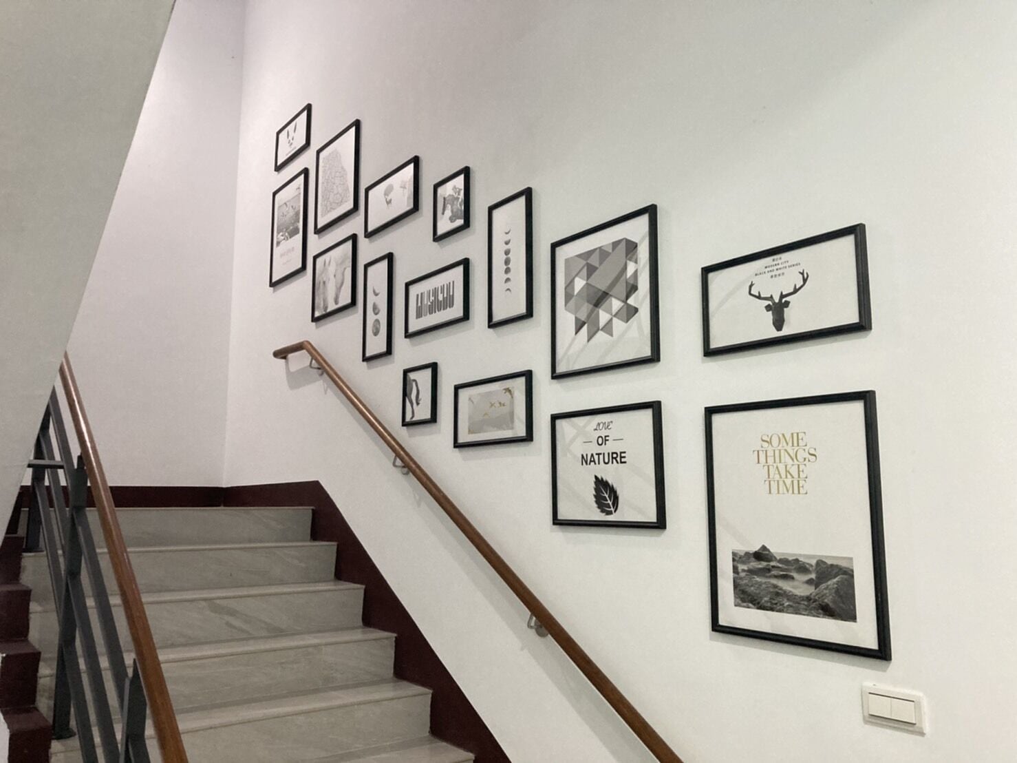 Un escalier avec une main courante en bois mène à un palier où plusieurs œuvres d’art encadrées sont exposées sur le mur.