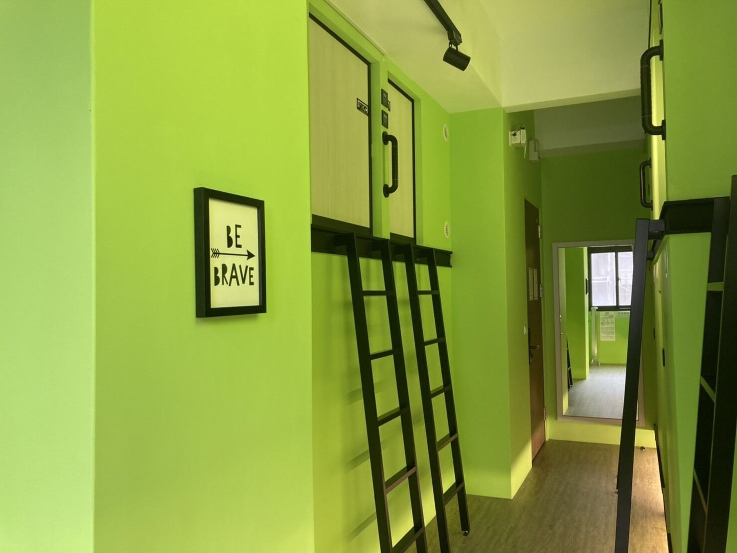 A hallway with green walls, a framed motivational quote, and a black ladder leaning against the wall.