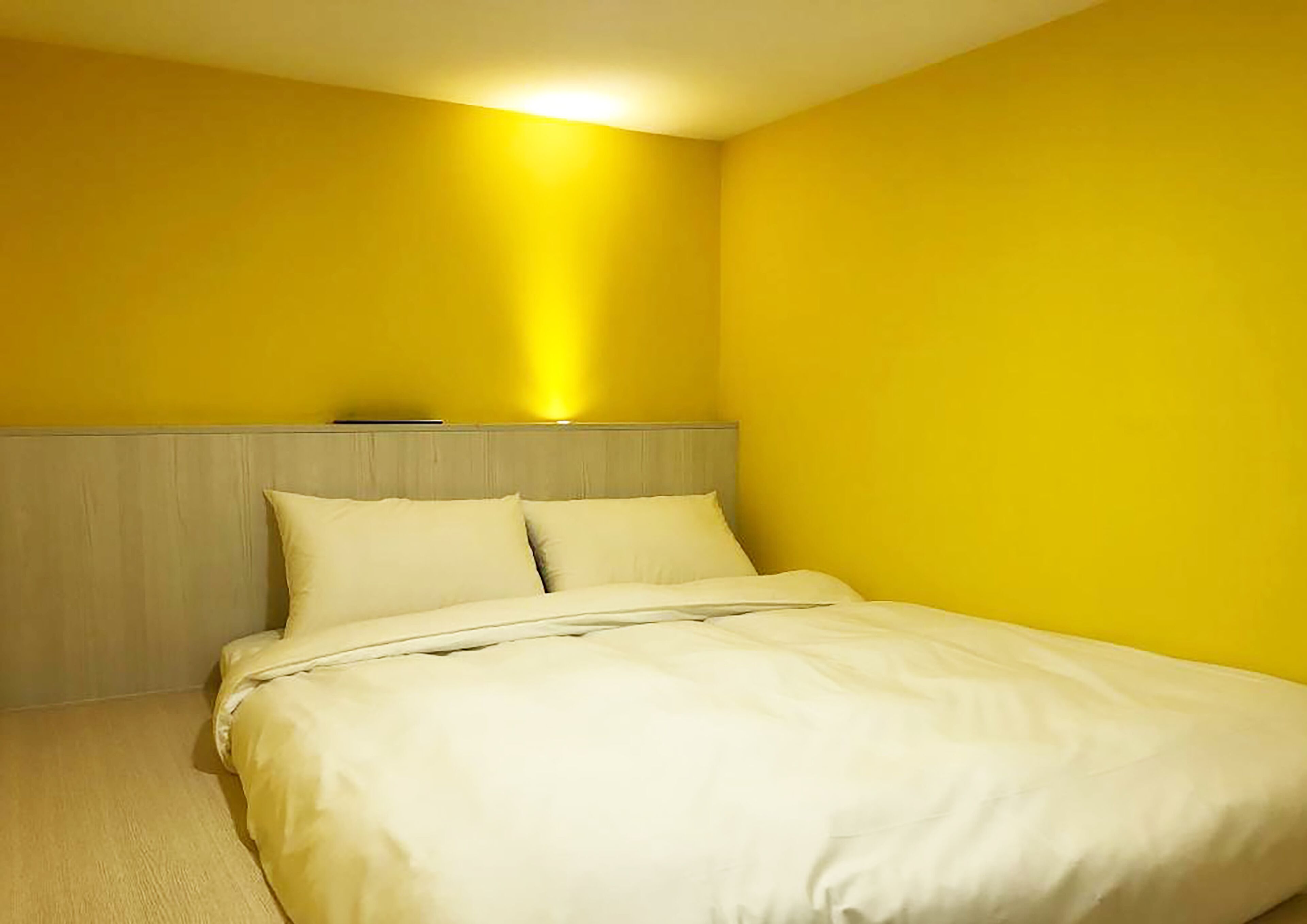 A bedroom with a bed, a headboard, and yellow walls.