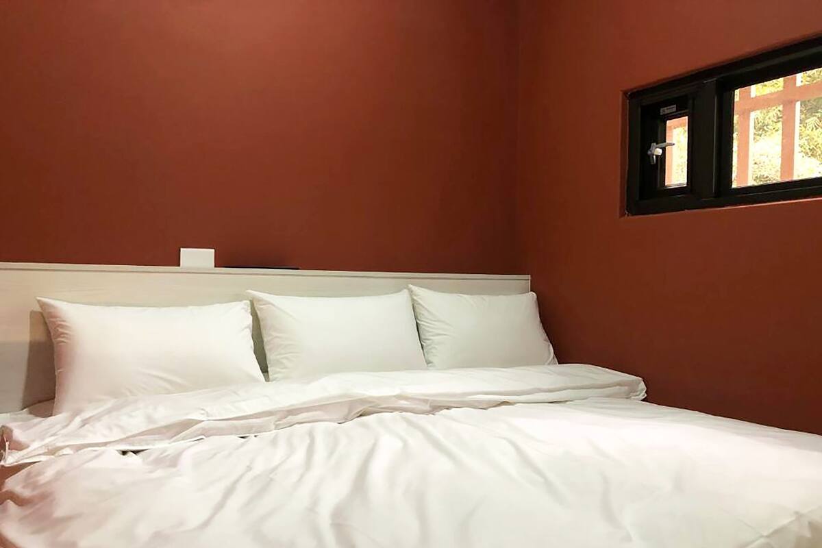 A bedroom with a bed, white bedding, and a window with a view of greenery.