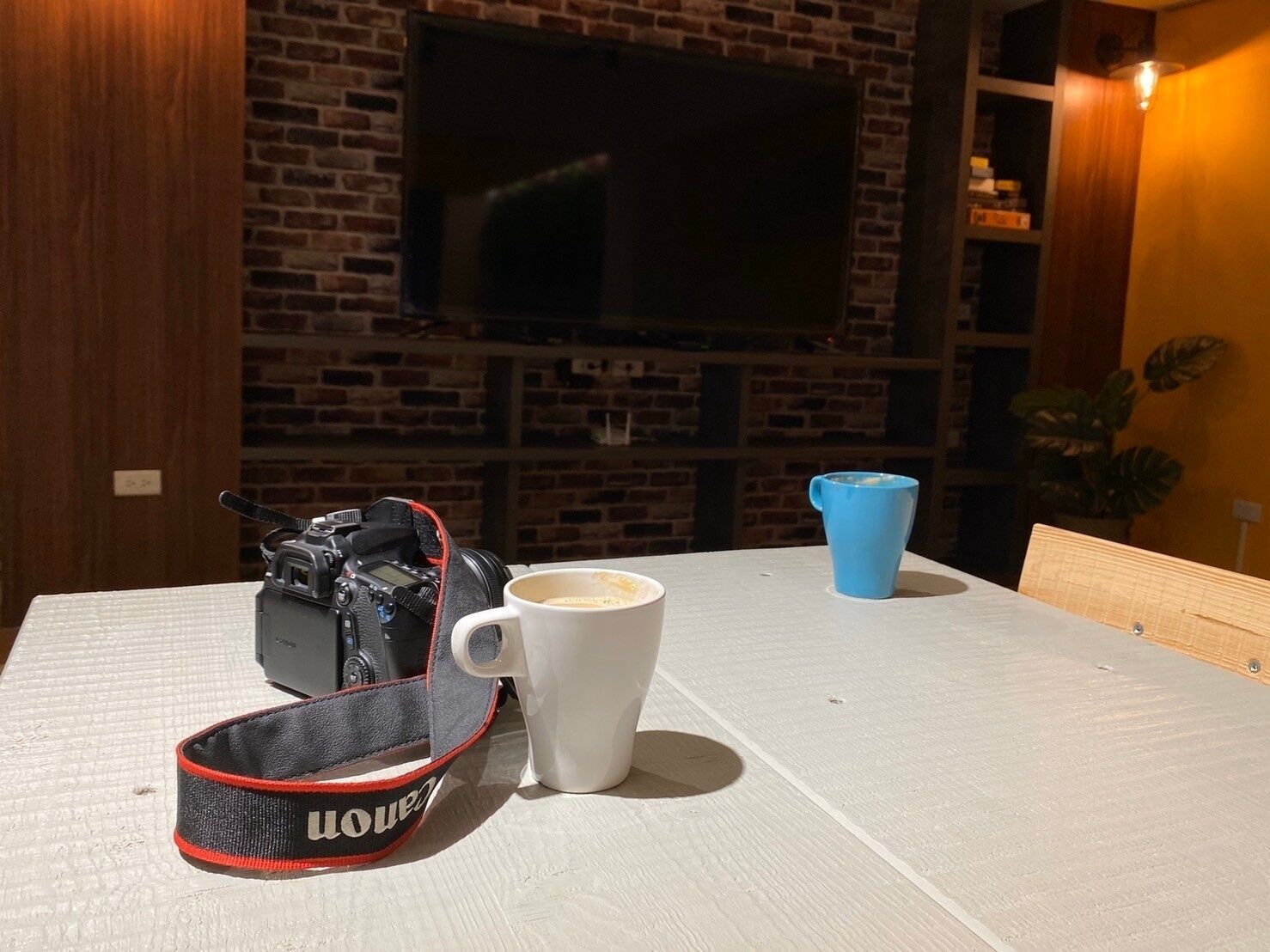Una mesa con una cámara, una taza blanca y una taza azul.