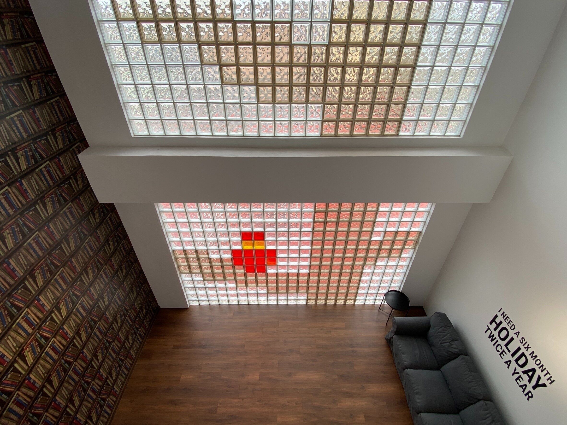 Una habitación moderna con piso de madera, un sofá negro, una estantería y un ventanal con diseño geométrico.