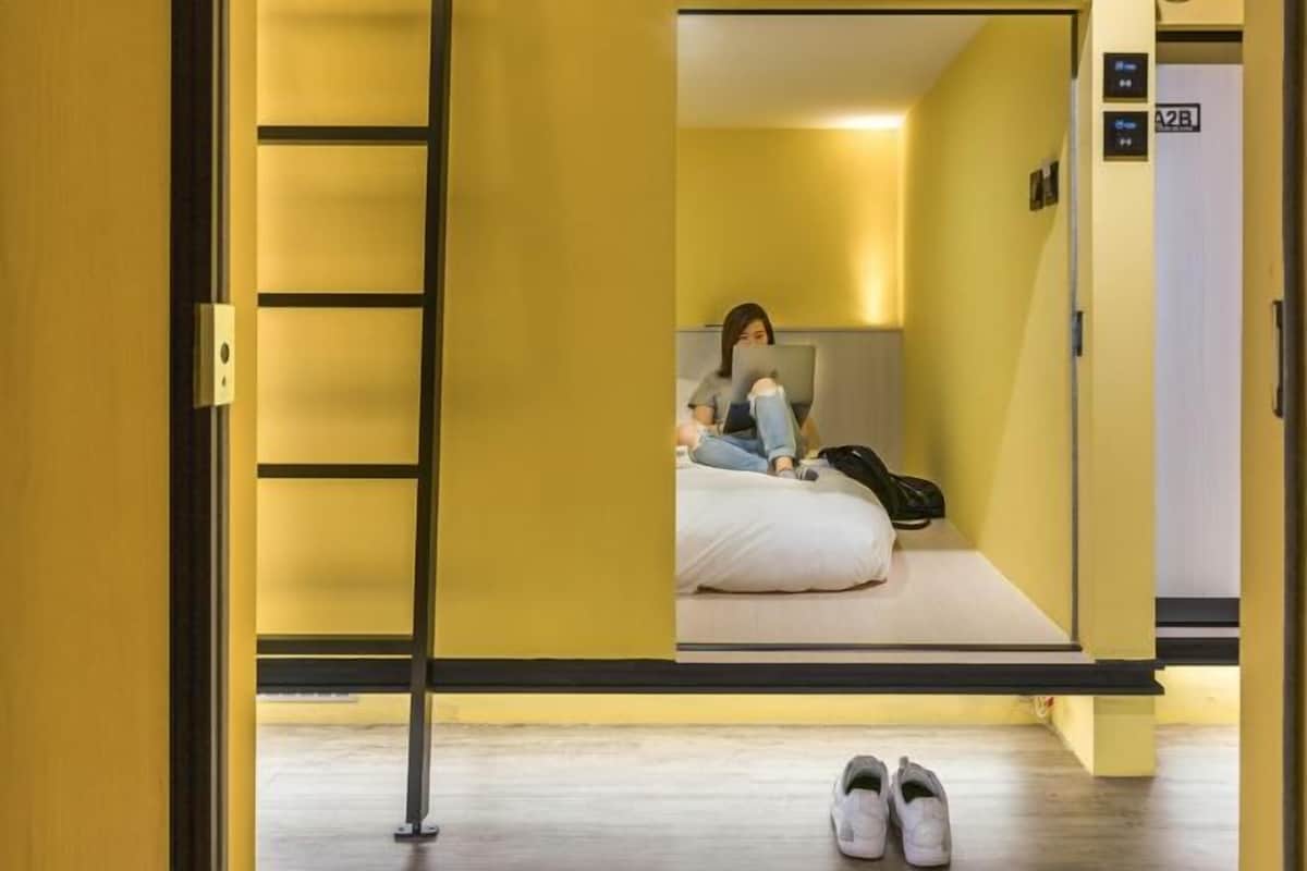 Quarto de hotel com uma cama, uma pessoa sentada na cama e um par de sapatos no chão.