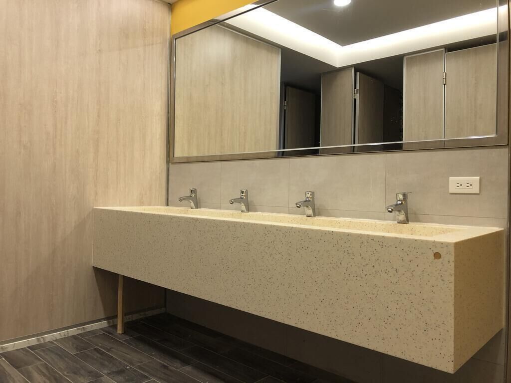 A modern bathroom with a long, speckled vanity, three faucets, and a large mirror above the sink.