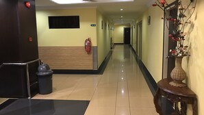 A hotel corridor with a fire extinguisher, a trash bin, a ceiling fan, and a decorative vase with flowers. - Sipadan Inn 1 (Semporna)
