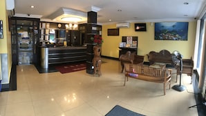A hotel lobby with a reception desk, a coffee machine, a clock, a wall-mounted TV, a bench, and a large window. - Sipadan Inn 1 (Semporna)