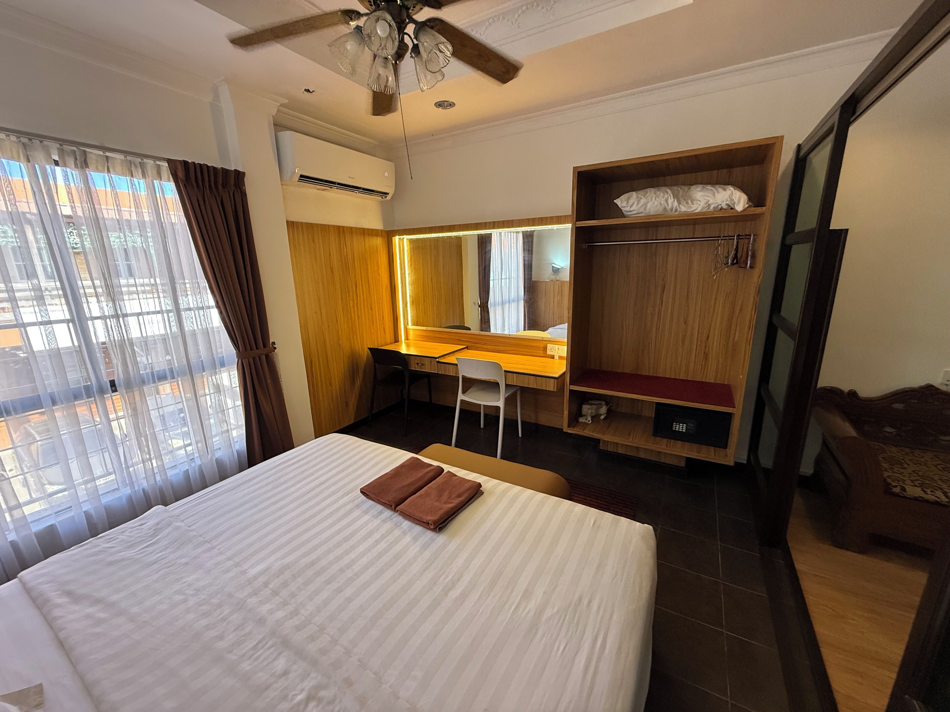 Ein Hotelzimmer mit Bett, Schreibtisch, Stuhl, Kleiderschrank und Deckenventilator.