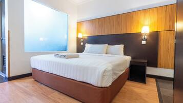 A modern hotel room with a large bed, wooden headboard, two bedside lamps, and a large window.