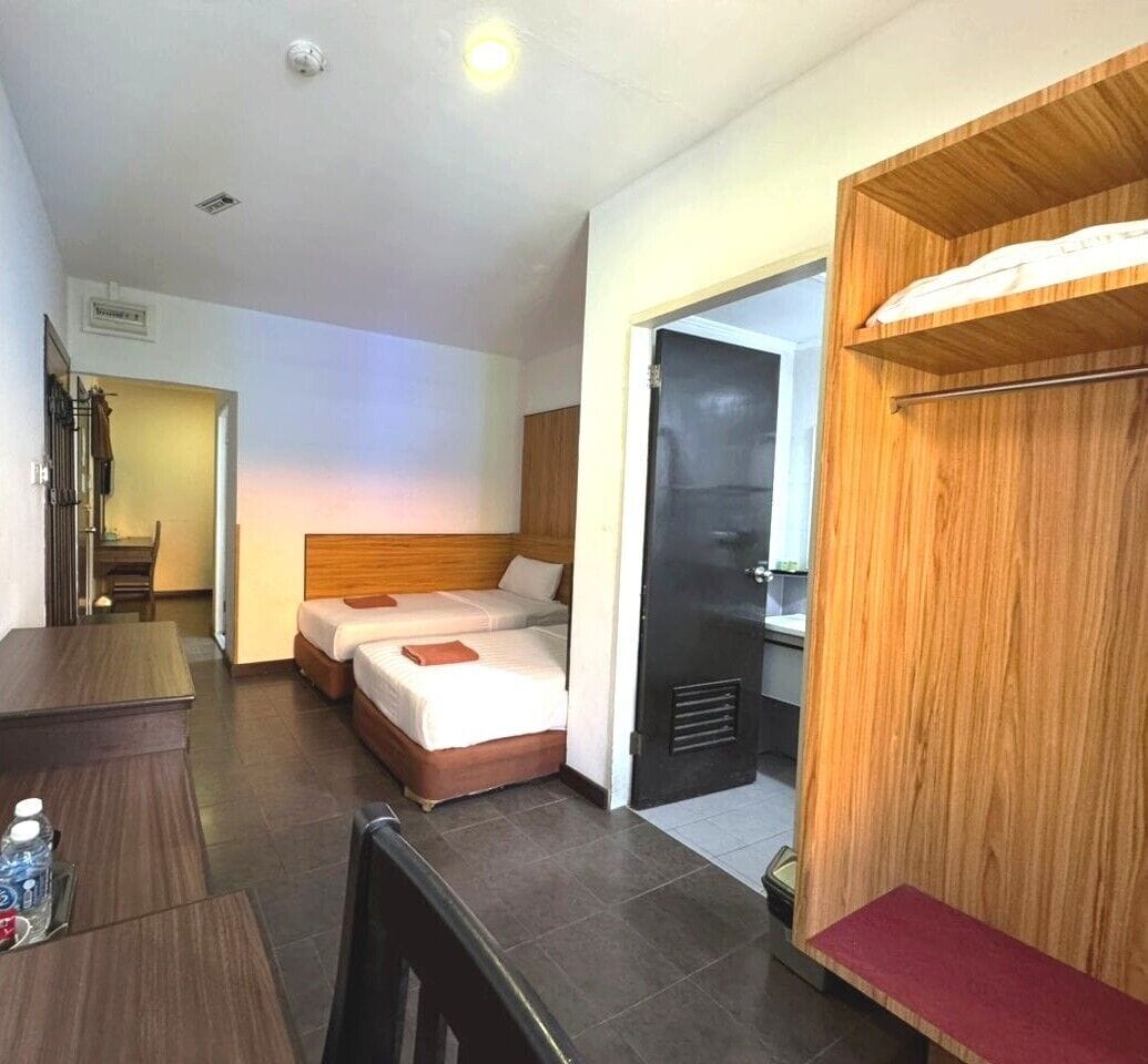 Habitación de hotel con dos camas, un armario de madera, un escritorio con silla y una mesita con una botella de agua.