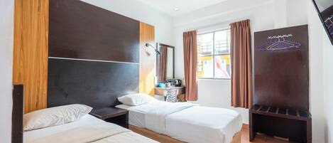 Habitación de hotel con dos camas, un cabecero de madera, un escritorio pequeño con espejo, una ventana con cortinas y un televisor en la pared.