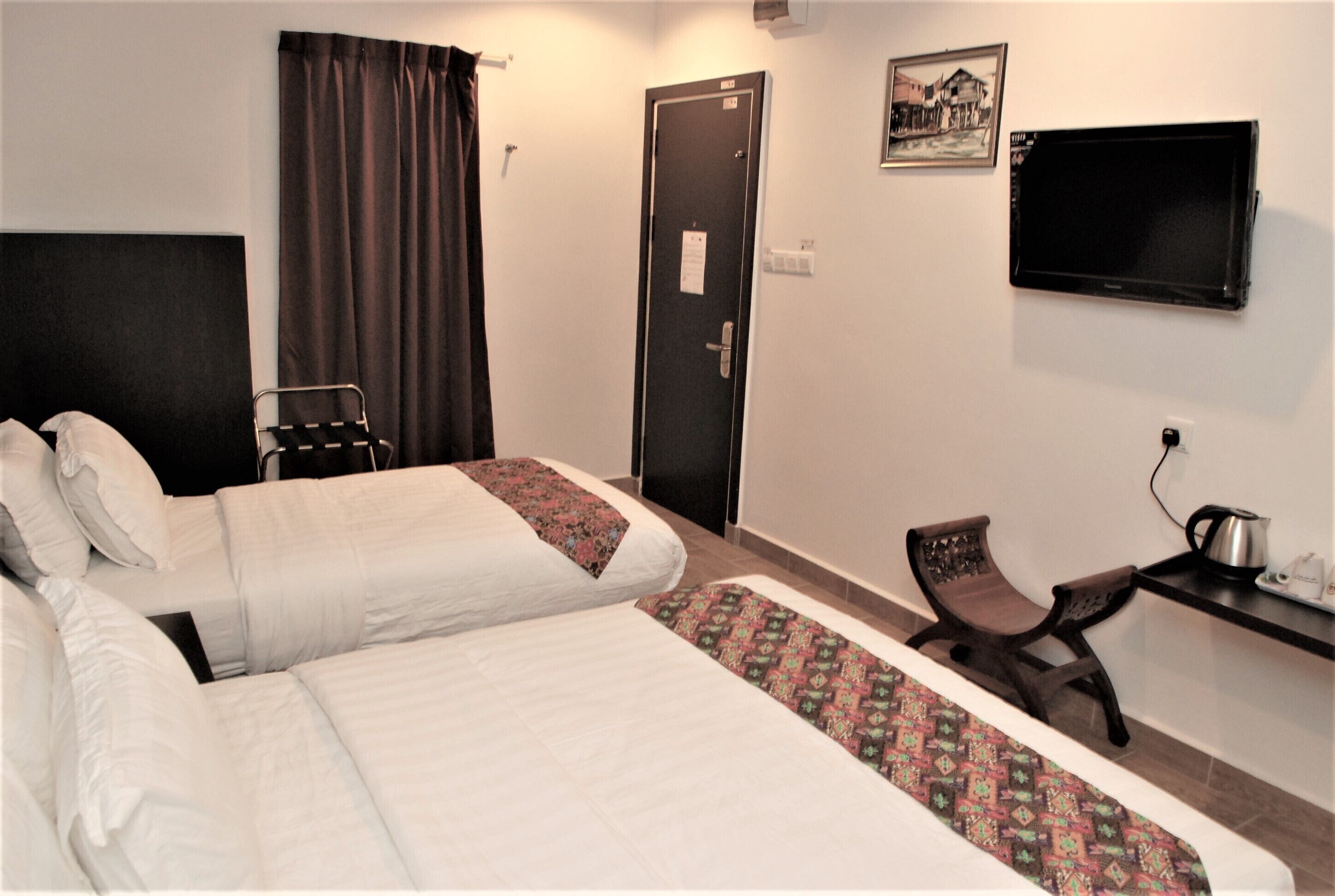 A hotel room with two beds, a desk with a chair, a television, and a door.