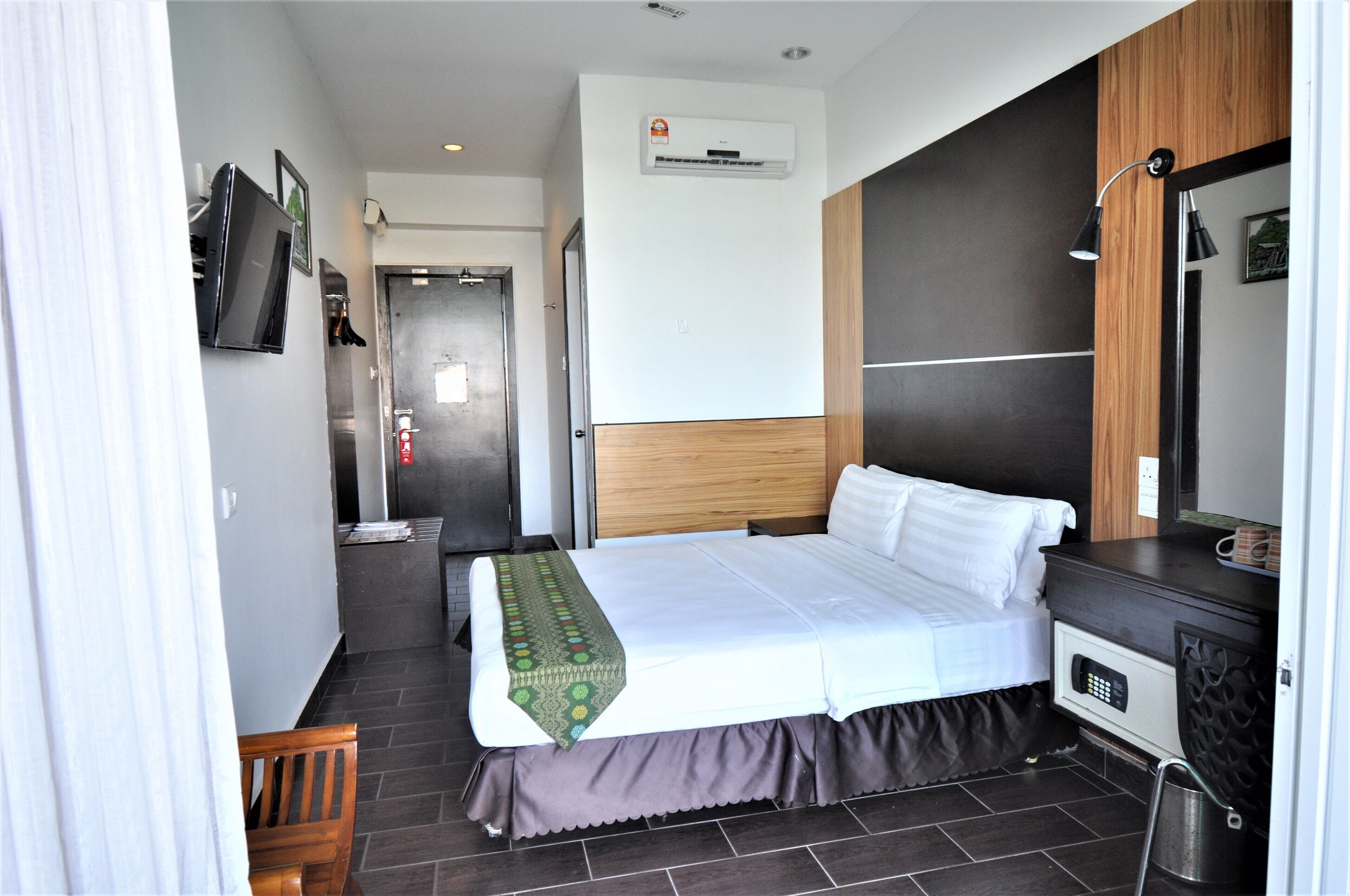 A hotel room with a bed, a desk, a chair, an air conditioning unit, and a television.