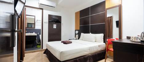 A hotel room with a bed, a desk, a chair, a TV, and an air conditioning unit.