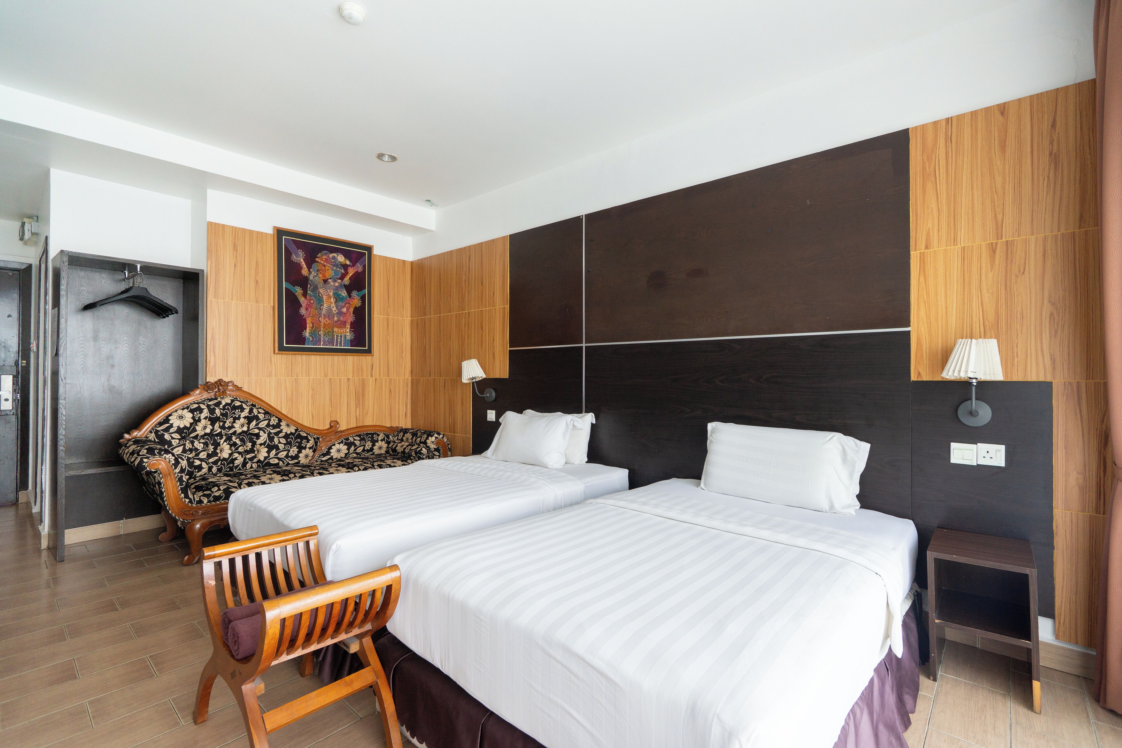 A hotel room with two beds, a wooden bench, a sofa, and a small table.