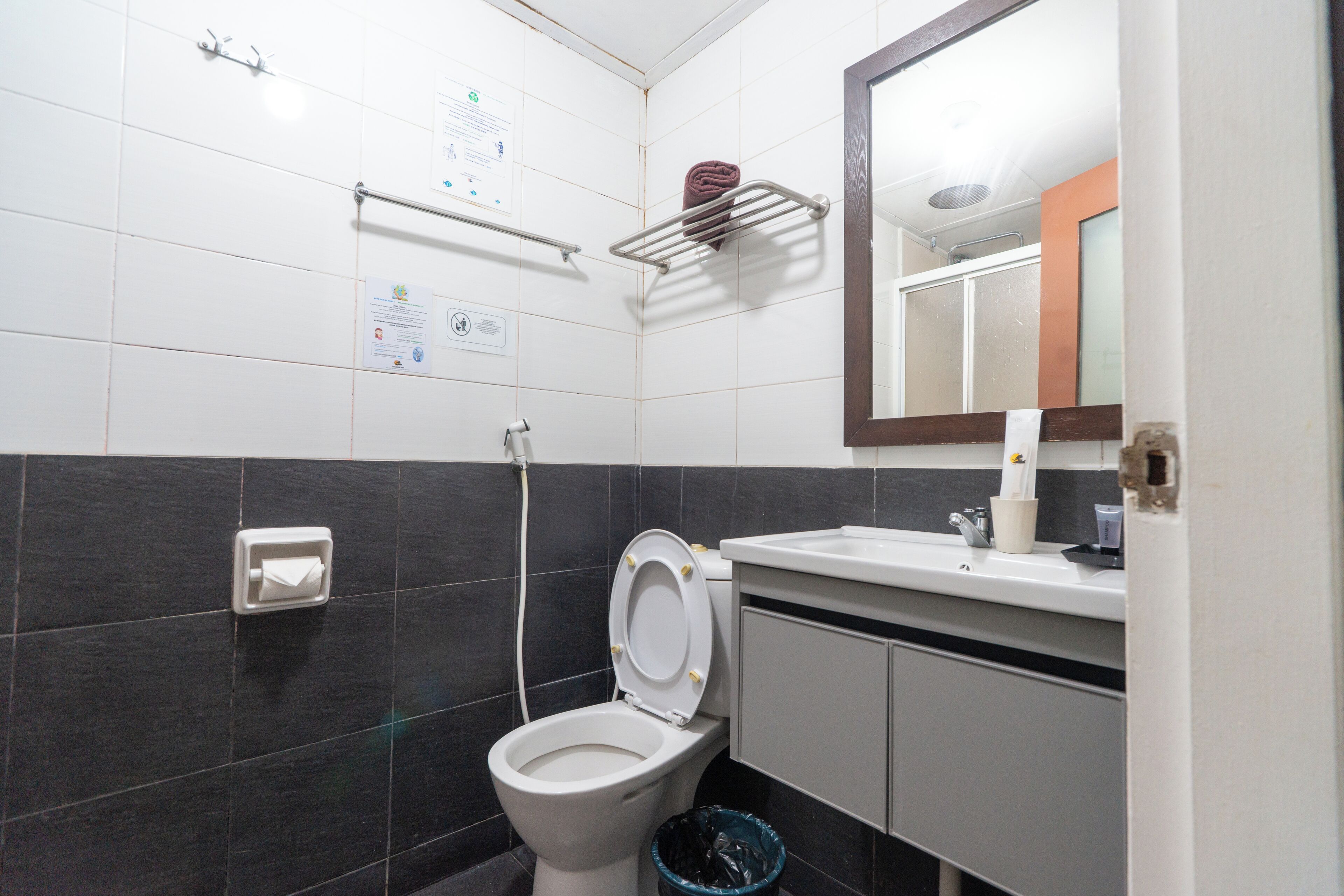 A bathroom with a toilet, sink, mirror, towel rack, and a trash bin.