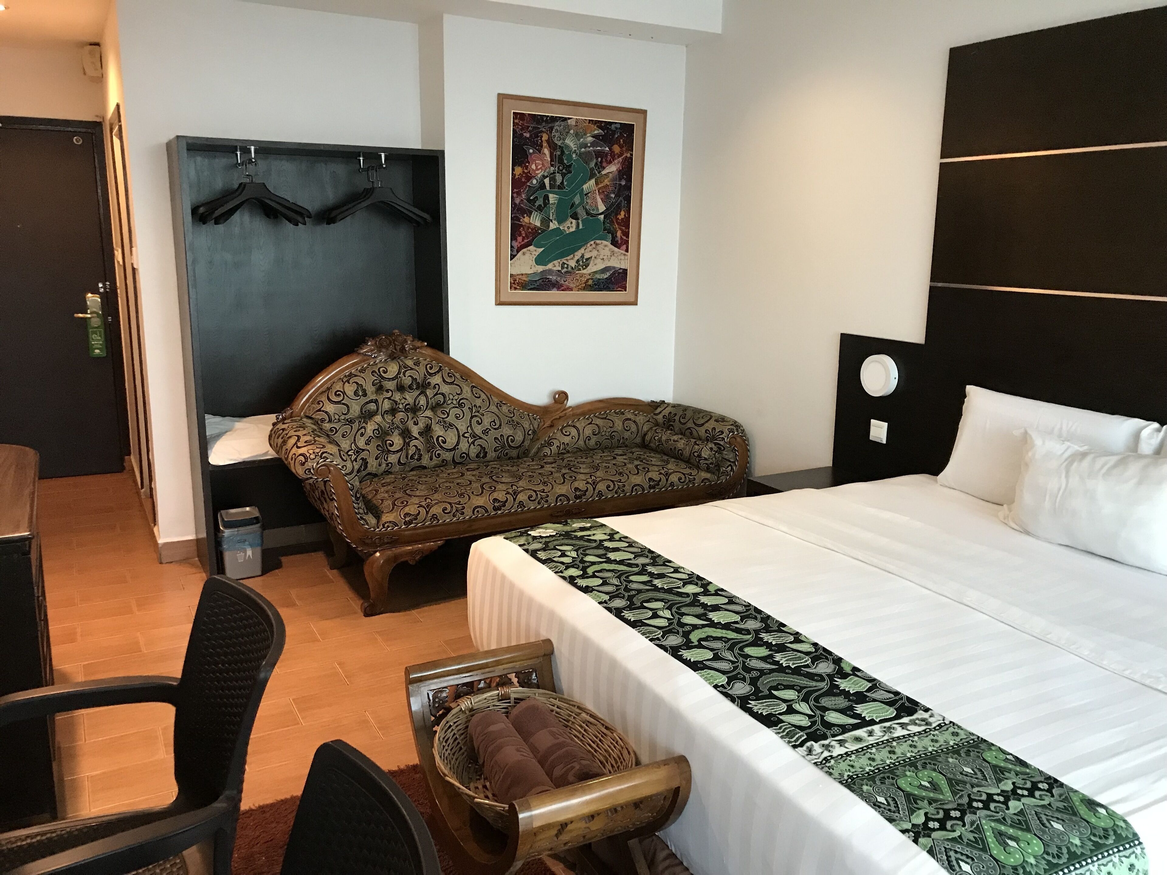 Een hotelkamer met een bed, een bank, een stoel, een kleine tafel en een kapstok aan de muur.