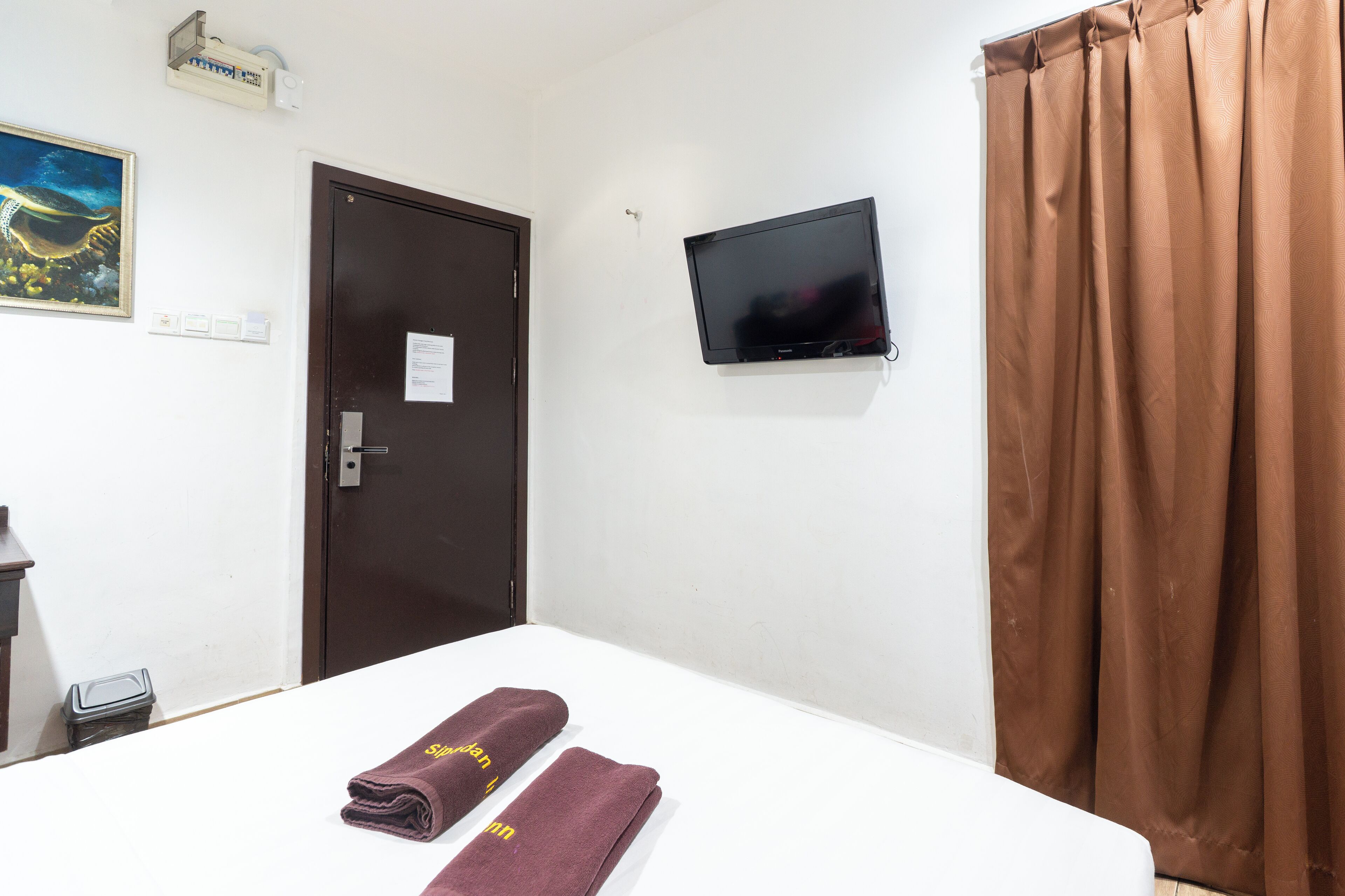 A hotel room with a bed, a TV mounted on the wall, a door, and a curtain.