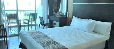 A hotel room with a large bed, a desk with a mirror, and a chair. There is a balcony with chairs and a table.