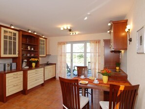 A kitchen with wooden cabinets, a dining table with chairs, and a window with curtains.
