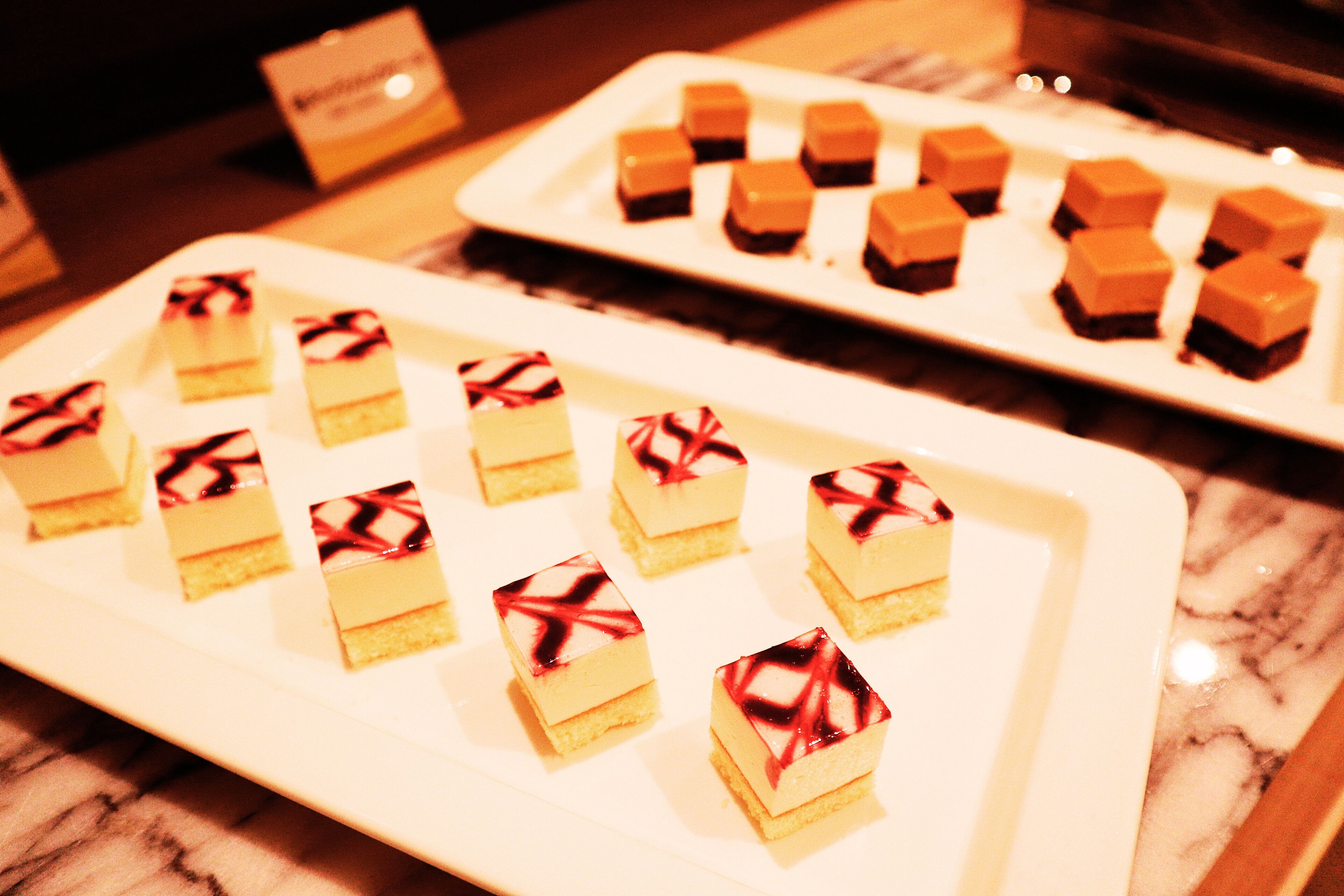 A dessert display with various square-shaped desserts on white plates.