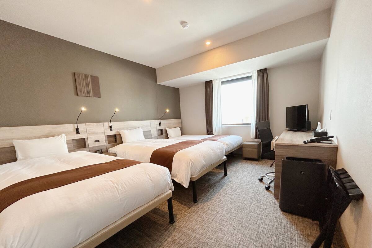 Habitación de hotel con dos camas, un escritorio, un televisor y una ventana con cortinas.