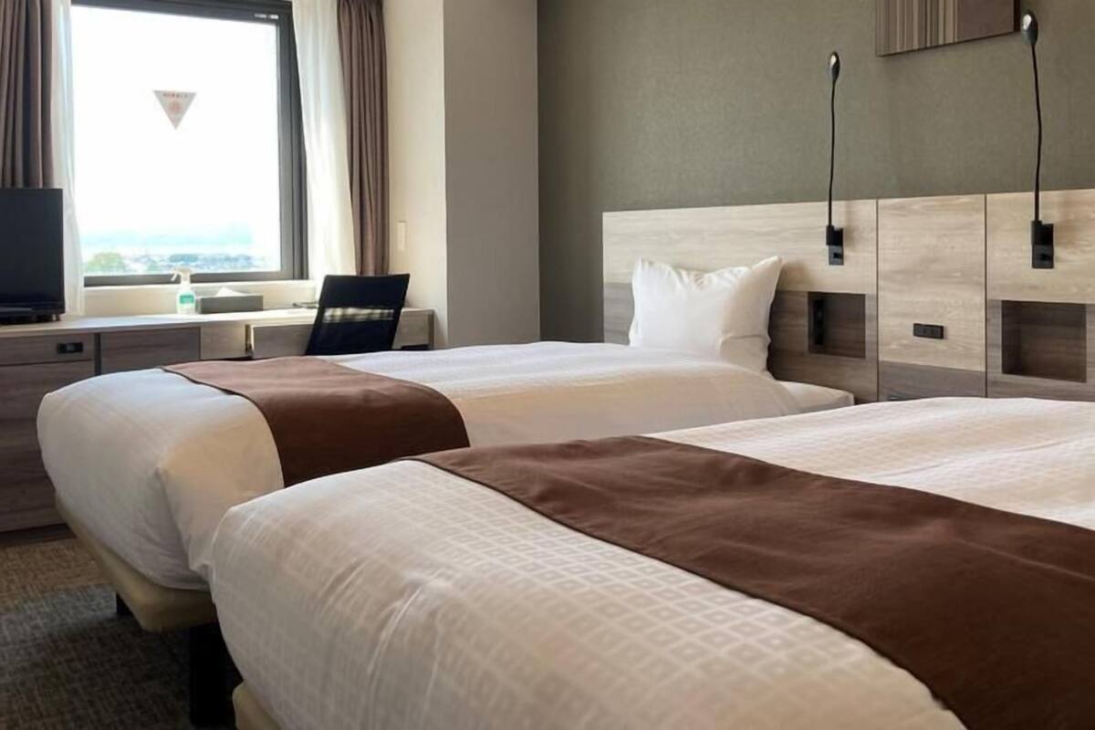 Una habitación de hotel con dos camas, televisión, escritorio y ventana con cortinas.