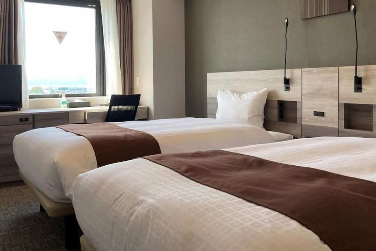 Quarto de hotel com duas camas, televisão, secretária e janela com cortinas.