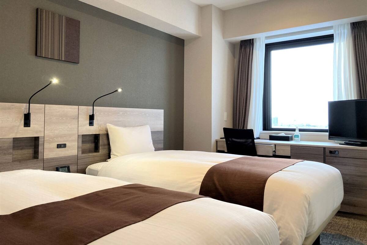 Habitación de hotel con dos camas, un escritorio, un televisor y una ventana con cortinas.