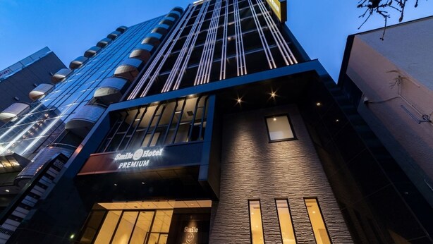 Un moderno edificio de hotel con un llamativo letrero que dice 'Smile Hotel Premium', que presenta un diseño elegante con ventanas de vidrio reflectante y fachada texturizada.