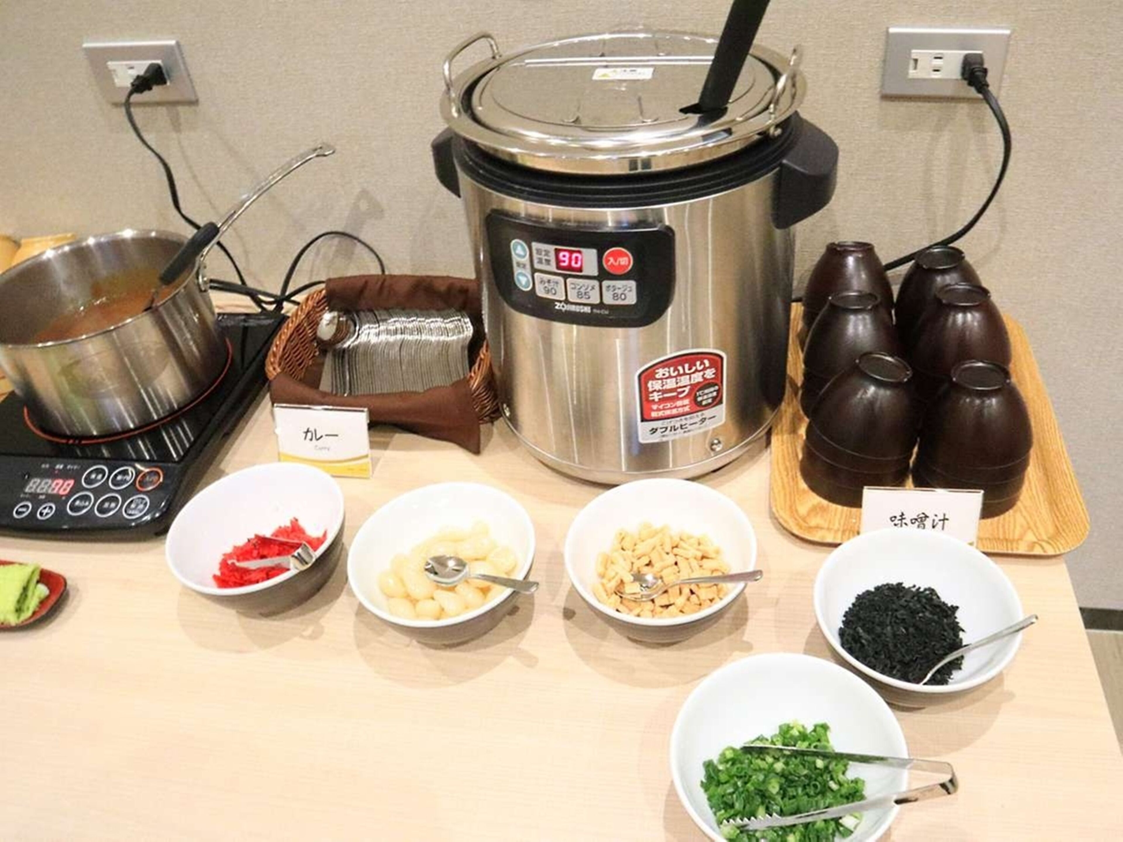 Un área de cocina con una cocedora de arroz, una olla en la estufa y varios cuencos con comida.