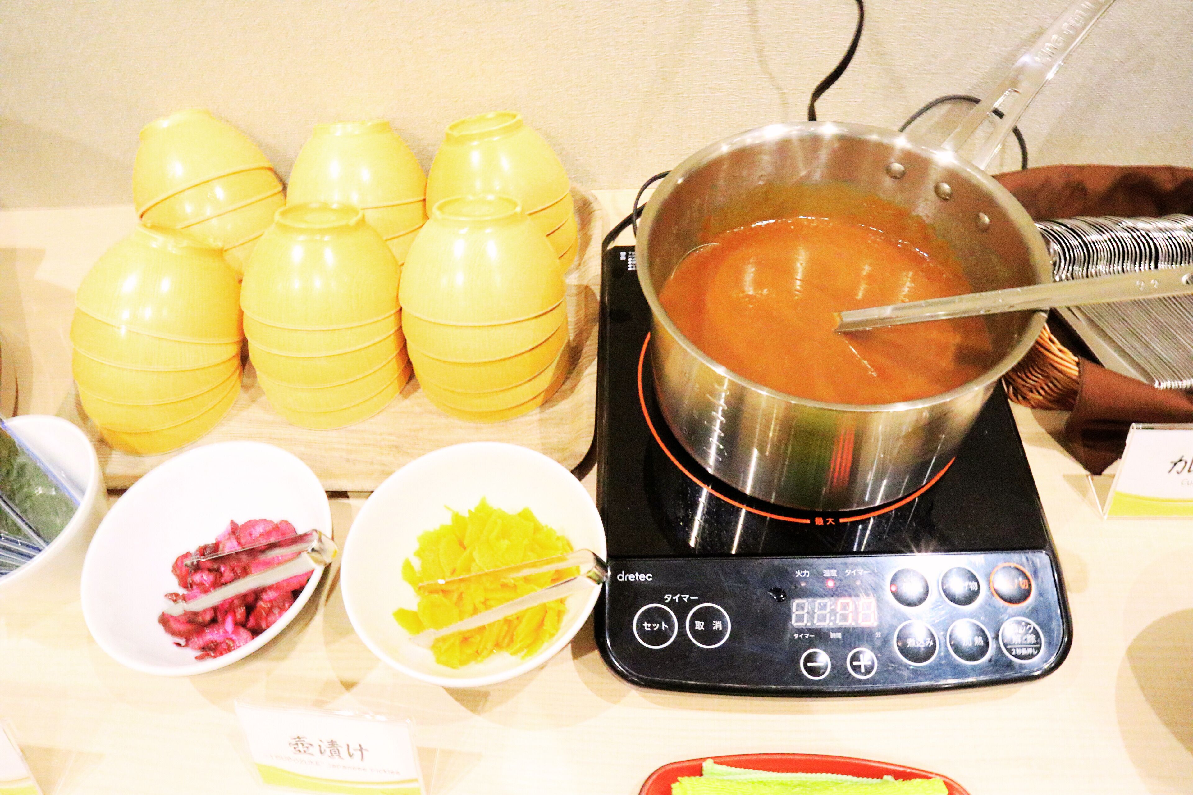 A table with a pot of soup, yellow containers, and bowls with food items.