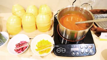 A table with a pot of soup, yellow containers, and bowls with food items.