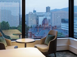 Habitación de esquina con dos sillones y una mesita, con vista a un paisaje urbano que combina edificios modernos y históricos.