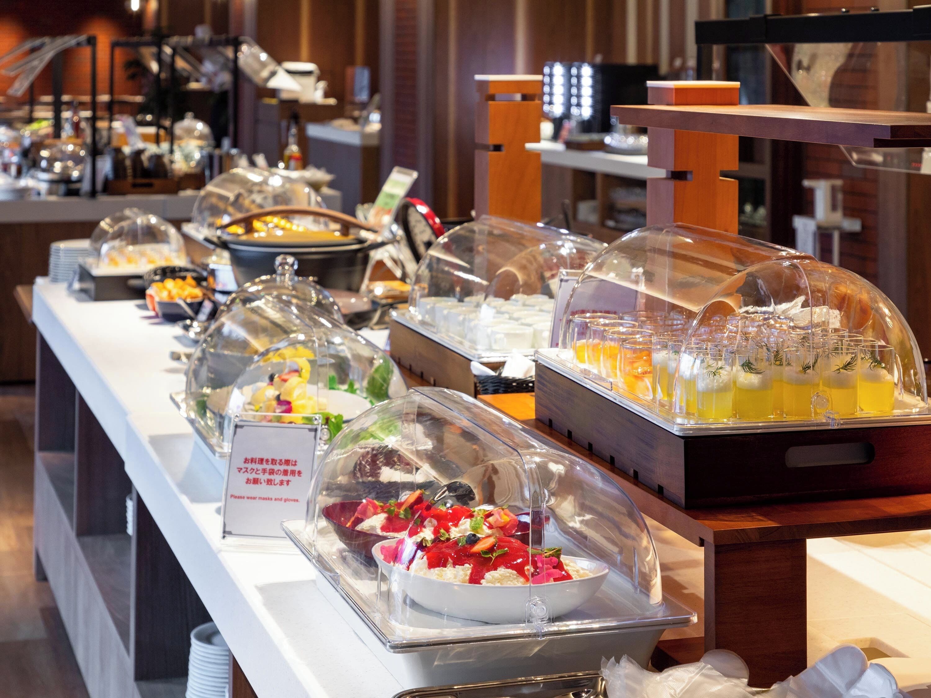 A buffet with various food items covered in glass domes, including fruits, vegetables, and beverages.