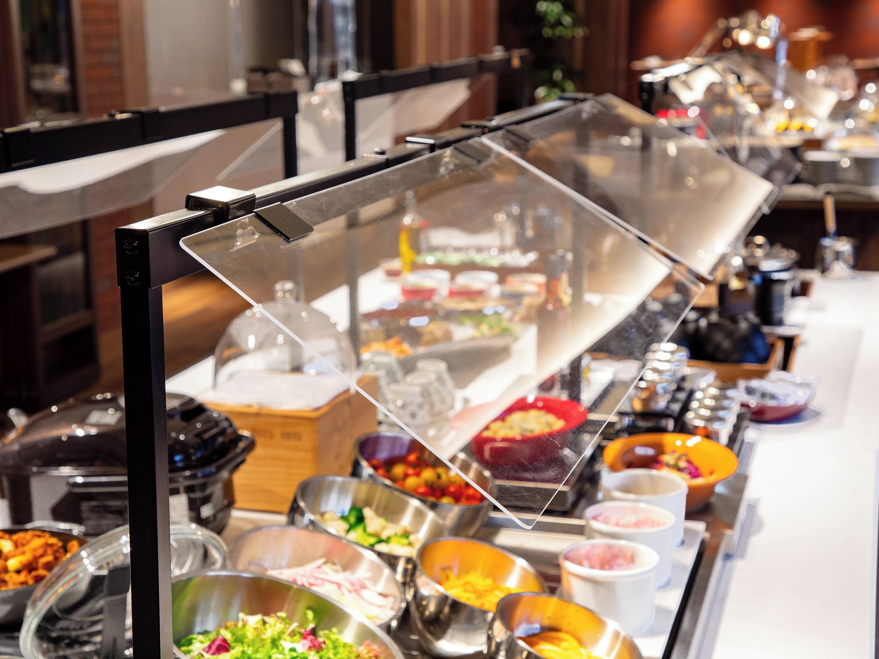 A buffet with various food items and a clear protective barrier.